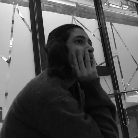 Gabriela resting her chin on her hand by a window, in black and white, during the bootcamp.