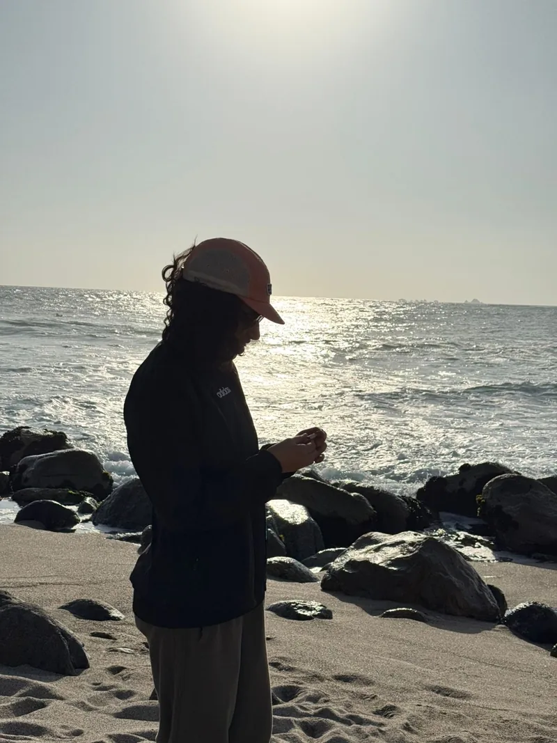 Gabriela standing on a rocky beach beside the sea.