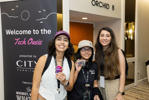 Gabriela and two other attendees at the Tech Oasis entrance, holding React Miami stickers.