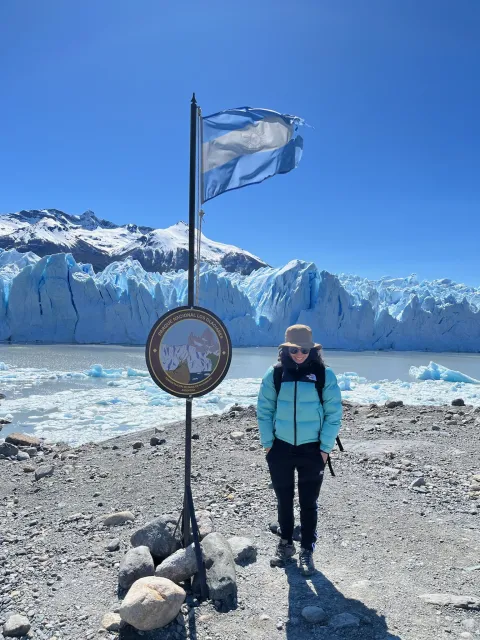 Standing beside Perito Moreno Glacier in Los Glaciares National Park, Argentina, with the Argentine flag flying overhead.